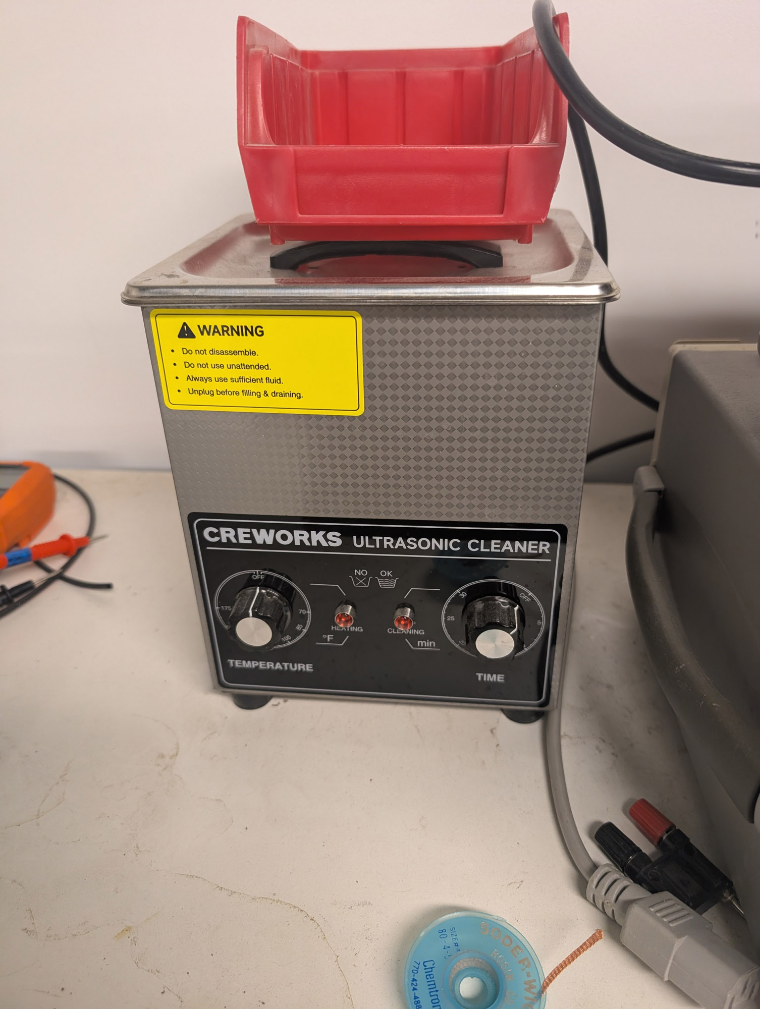 A metal boxy device with a handle to lift a cover off the top, a mostly-metal front with a black control panel near the bottom. The panel has knobs for Temperature and Time, and LEDs for Heating and Cleaning.